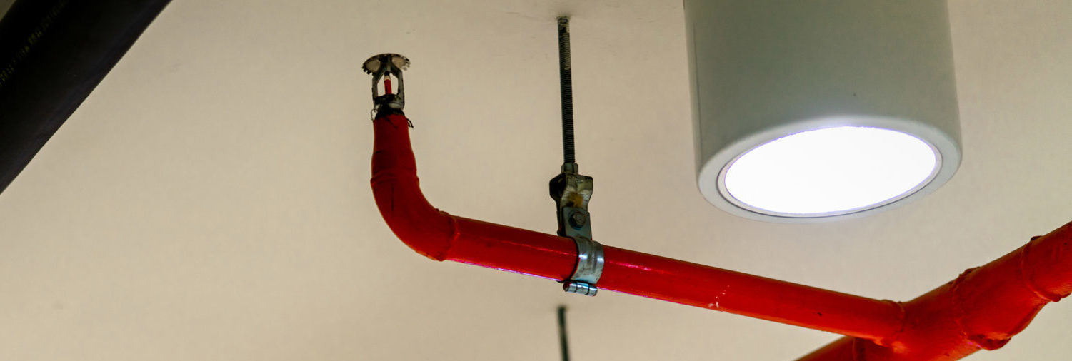 Automatic fire sprinkler safety system and black water cooling supply pipe. Fire Suppression. Fire protection and detector. Fire sprinkler system with red pipes hanging from ceiling inside building.