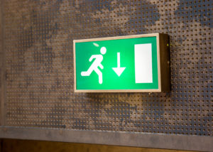 green fire exit sign that is lit up used in buildings 