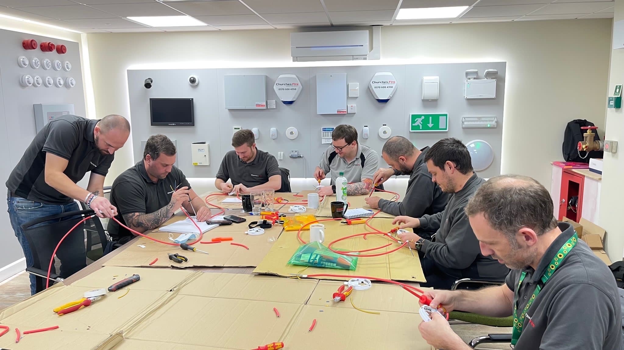 a group of adult men sitting working on demo fire alarms in a training session